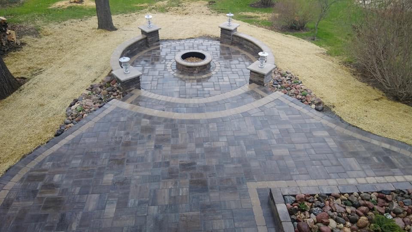 Circular paver courtyard with built-in fire pit and illuminated stone pillars